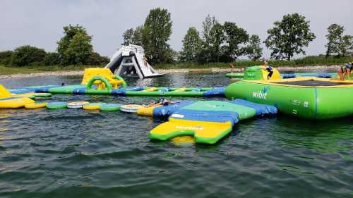 A colorful water park with inflatable structures on a lake, featuring slides and obstacle courses.