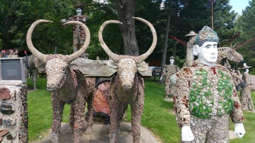 A whimsical outdoor sculpture featuring two stone bulls and a colorful figure, surrounded by trees and greenery.