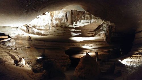 A dimly lit cave interior with rock formations, stalactites, and a staircase leading into the depths.