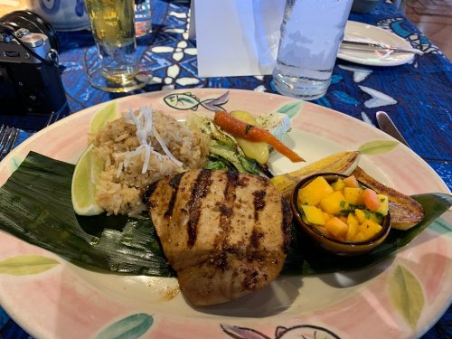 Grilled fish fillet served with rice, vegetables, plantains, and mango salsa on a decorative plate.