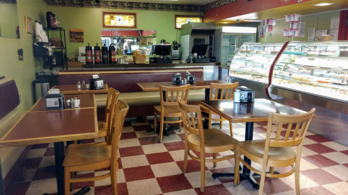 A cozy diner interior with wooden tables and chairs, a counter, and a display case filled with desserts.