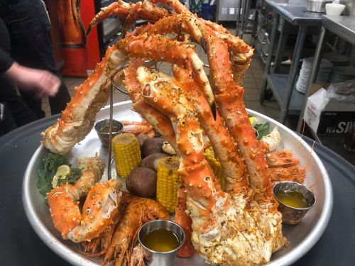 A large seafood platter featuring crab legs, shrimp, corn, and potatoes, served with dipping sauces.