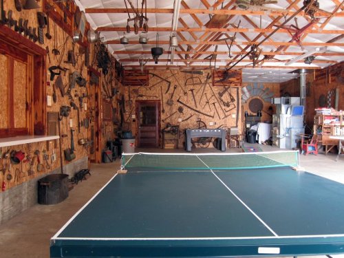 A spacious garage with a ping pong table and walls adorned with various vintage tools and equipment.