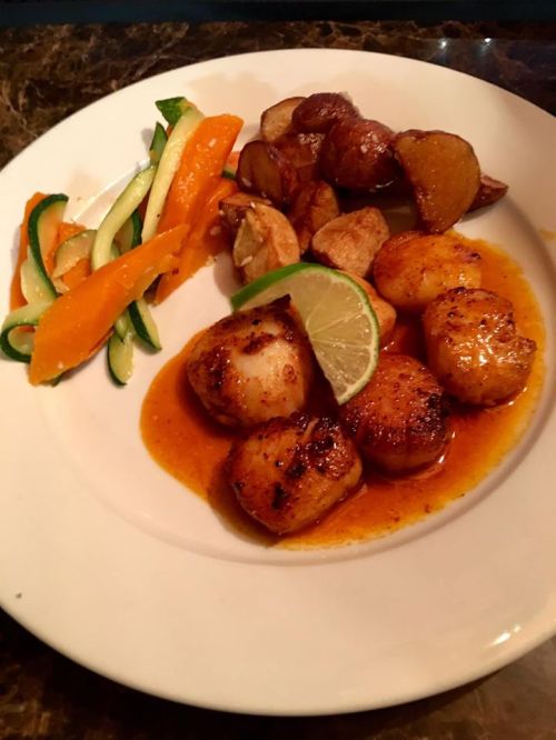 A plate of seared scallops with lime, roasted potatoes, and colorful vegetable ribbons.
