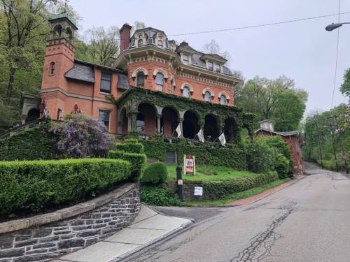 A large, ivy-covered mansion with a red brick facade, surrounded by greenery and a winding road.