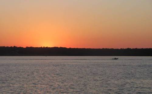 A serene sunset over a calm lake, with a silhouette of a small boat in the distance.