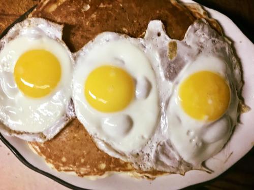 A plate with three sunny-side-up eggs on top of a large pancake.
