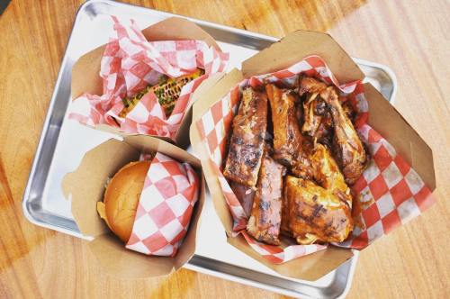 A tray with barbecue ribs, a sandwich, and corn on the cob, all wrapped in red and white checkered paper.