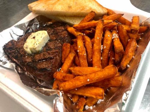 A plate featuring a grilled steak topped with butter, served with crispy sweet potato fries and toasted bread.