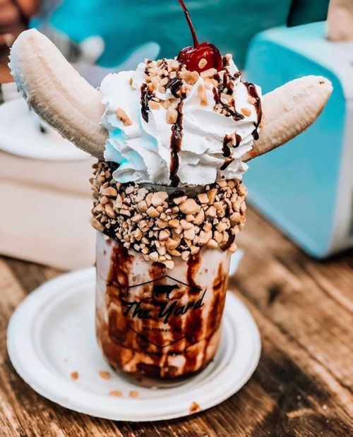 A decadent milkshake topped with whipped cream, banana slices, nuts, chocolate drizzle, and a cherry.