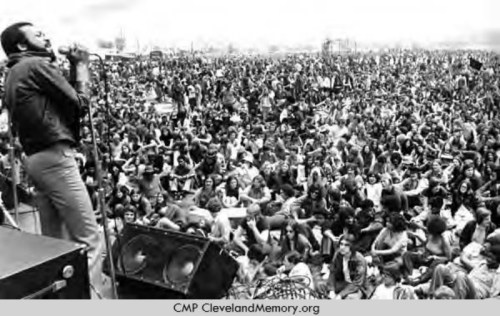 A singer performs on stage in front of a large crowd at an outdoor music festival.