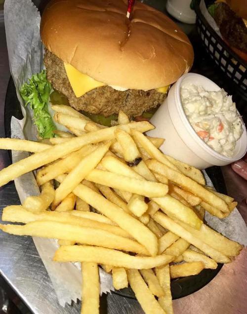 A plate featuring a cheeseburger with lettuce, pickles, fries, and a side of coleslaw in a cup.