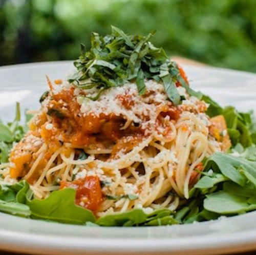 A plate of spaghetti topped with tomato sauce, fresh basil, and cheese, served on a bed of arugula.