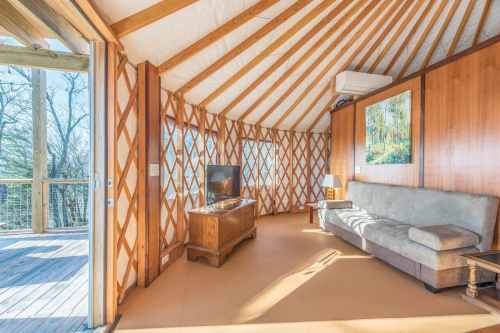 Cozy interior of a yurt with wooden accents, a sofa, TV, and large windows letting in natural light.