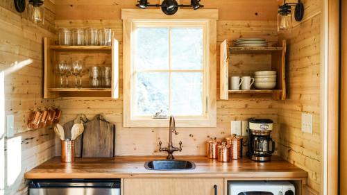 Cozy kitchen with wooden walls, shelves of glassware, a sink, coffee maker, and a window letting in natural light.