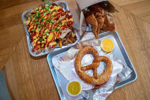 A tray with a large pretzel and cheese dip, alongside loaded fries topped with cheese, ketchup, and green onions.