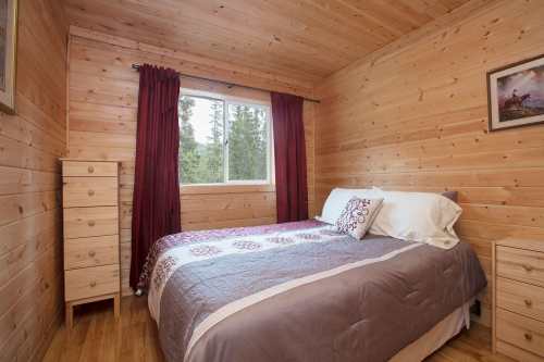 Cozy wooden bedroom with a double bed, red curtains, and a window overlooking trees.