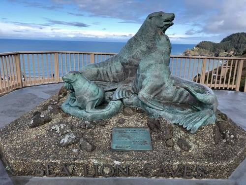 Bronze sculpture of sea lions on a rocky base, overlooking the ocean with a scenic view in the background.