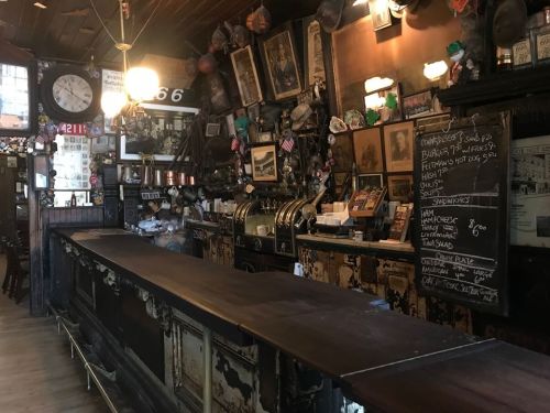 A vintage bar interior with a wooden counter, antique decor, and a chalkboard menu on the wall.