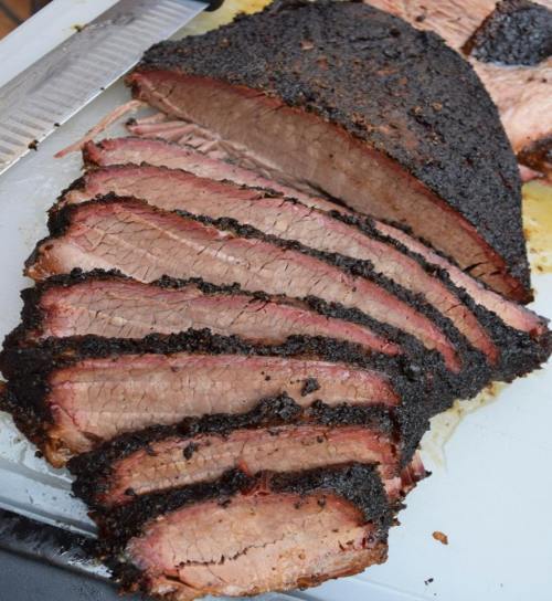Sliced smoked brisket with a dark, crusty exterior and tender pink interior on a cutting board.