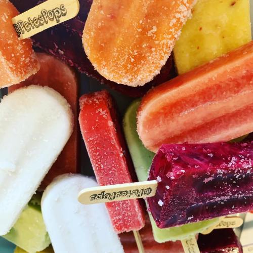 A colorful assortment of frozen popsicles in various flavors, displayed with wooden sticks.