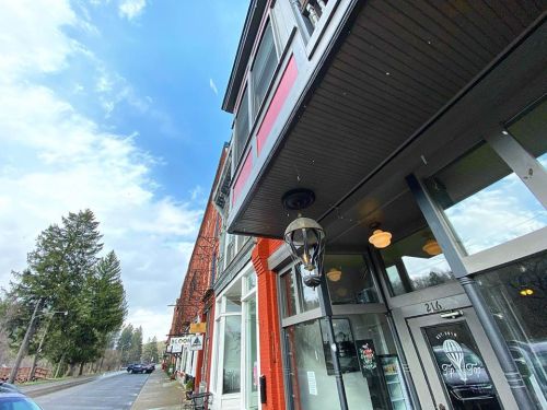 A street view of a quaint town with a red building, a shop entrance, and trees under a partly cloudy sky.