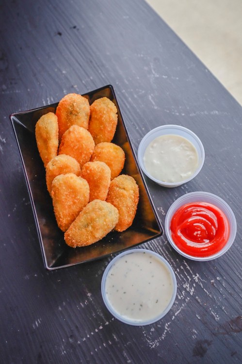 A black plate with golden-brown fried snacks and three dipping sauces: ranch, ketchup, and a creamy sauce.