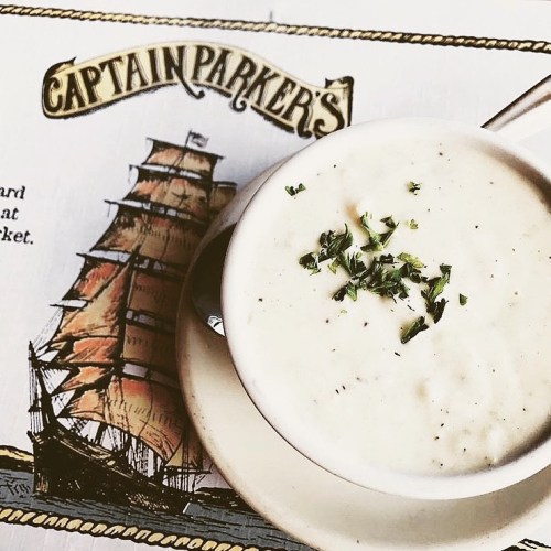 A bowl of creamy soup garnished with herbs, placed on a menu featuring a ship illustration.