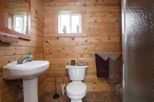 Cozy wooden bathroom featuring a sink, toilet, shower, and a small window for natural light.