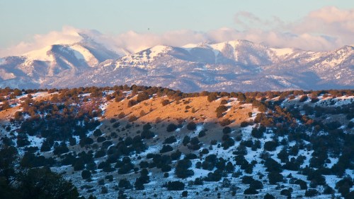 Snow-capped mountains rise in the background, with rolling hills and scattered trees in the foreground.
