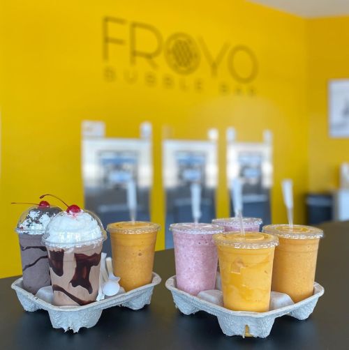 Two trays of colorful bubble tea drinks in clear cups, set against a bright yellow wall with "Frovo Bubble Bar" logo.