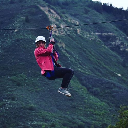 A person in a helmet and pink jacket zip-lining over a green mountainous landscape.
