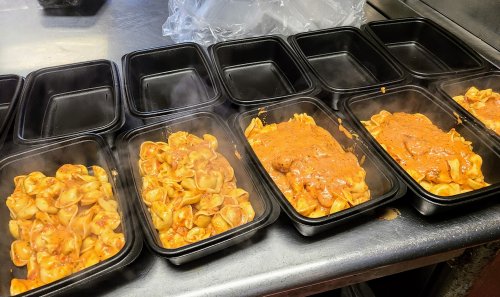Steaming pasta in black takeout containers, some with sauce and others plain, arranged on a kitchen counter.