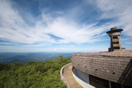 A scenic view from a circular observation tower surrounded by lush green mountains and a blue sky with clouds.