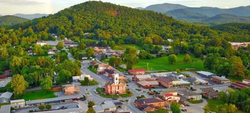 Aerial view of a small town surrounded by lush green hills and mountains, featuring a church and local buildings.