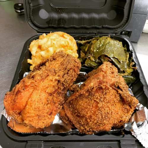 A takeout container with two pieces of fried chicken, macaroni and cheese, and collard greens.