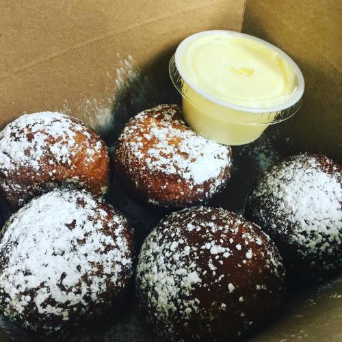 A box containing five powdered doughnuts and a small cup of yellow dipping sauce.