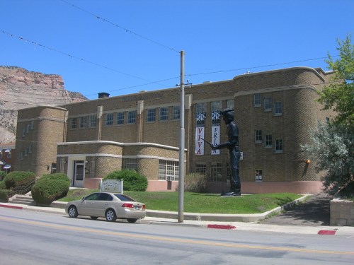 Historic brick building with a large statue outside, set against a clear blue sky and rocky hills in the background.