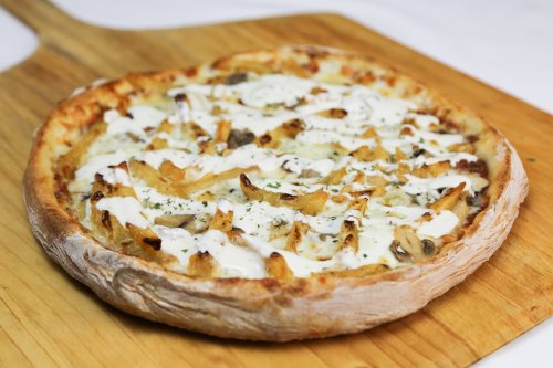 A freshly baked pizza topped with chicken, mushrooms, and drizzled with white sauce, resting on a wooden board.
