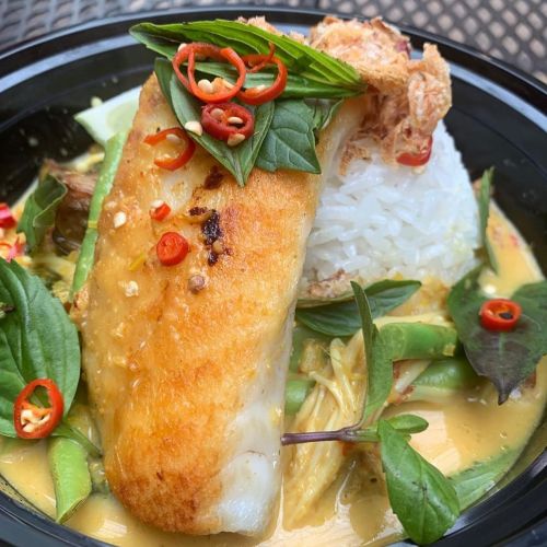 A bowl of rice topped with crispy fish, fresh herbs, and sliced red chilies in a flavorful sauce.