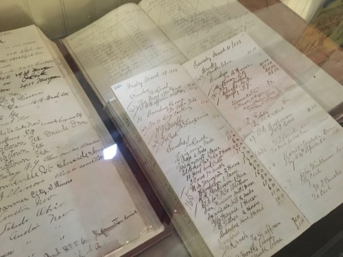Close-up of an open historical ledger with handwritten entries and dates, displayed under glass.