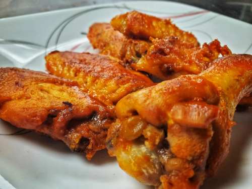 A close-up of crispy, golden-brown chicken wings on a white plate with a decorative design.