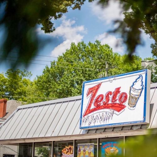 A colorful sign for Zesto ice cream shop, featuring a soft serve cone, with trees and a blue sky in the background.