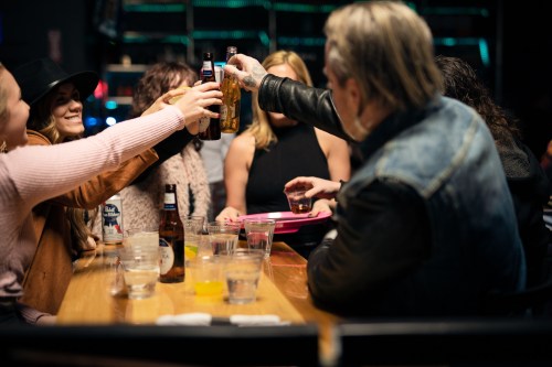 A group of people at a bar cheers with drinks, enjoying a lively social gathering.