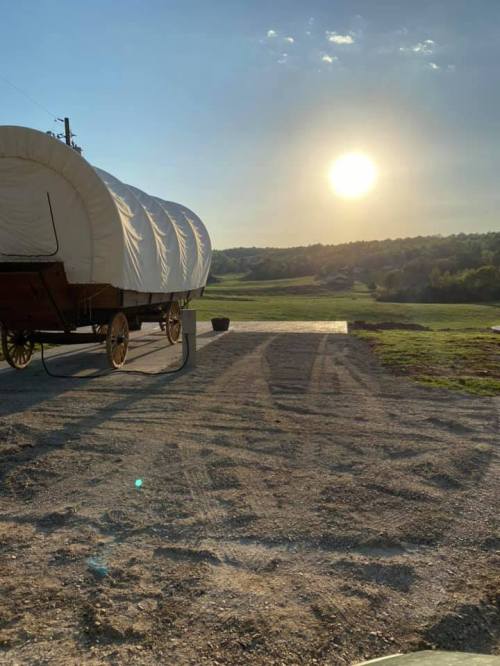 A covered wagon on a gravel path with a sunset over a green landscape in the background.