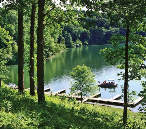 A serene lake surrounded by lush greenery, with a boat docked and people enjoying the peaceful scenery.