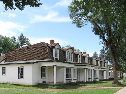 A row of white houses with sloped roofs, surrounded by green grass and trees under a blue sky.