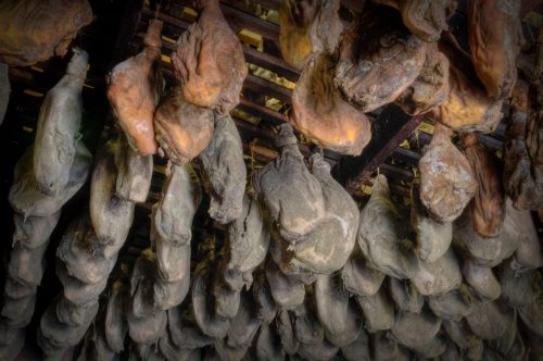 Cured hams hanging from wooden racks in a dimly lit storage area.