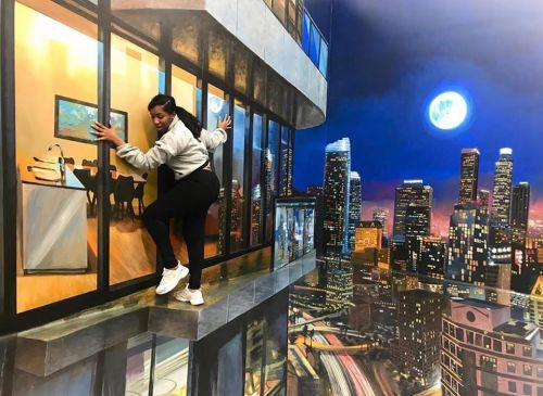A person poses on a painted ledge, creating an illusion of climbing outside a high-rise building at night.