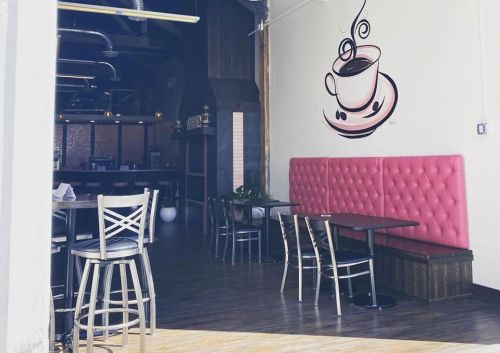 A cozy café interior featuring pink tufted seating, wooden tables, and a coffee cup mural on the wall.